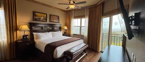 Habitación de hotel con una cama grande, un escritorio, un ventilador de techo y un balcón con vistas.