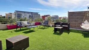 A rooftop patio with artificial grass, wicker furniture, a hanging chair, and potted plants.