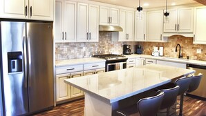 Cocina moderna con armarios blancos, electrodomésticos de acero inoxidable, una isla grande con taburetes y un salpicadero de piedra.