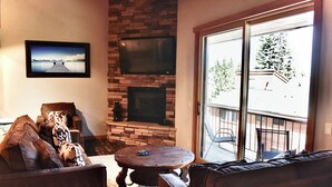 Un salón con chimenea, un televisor grande montado en la pared y vistas al exterior a través de una puerta corrediza de cristal.