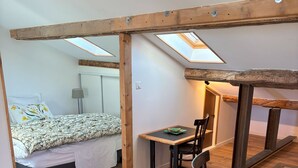 A bedroom with a bed, a bedside table, and a chair. There is a skylight above the bed and a table with chairs in the adjacent room. - Charming apartment in a private mansion in the center of Avignon (Avignon)