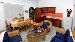 A compact living space with a dining area, a kitchen, and a seating area with wicker furniture and a glass coffee table.