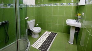 A bathroom with green tiles, a toilet, a sink, and a shower.