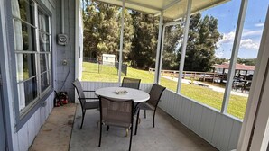 Une terrasse couverte avec une table ronde et quatre chaises, de grandes fenêtres et une vue sur l’extérieur.