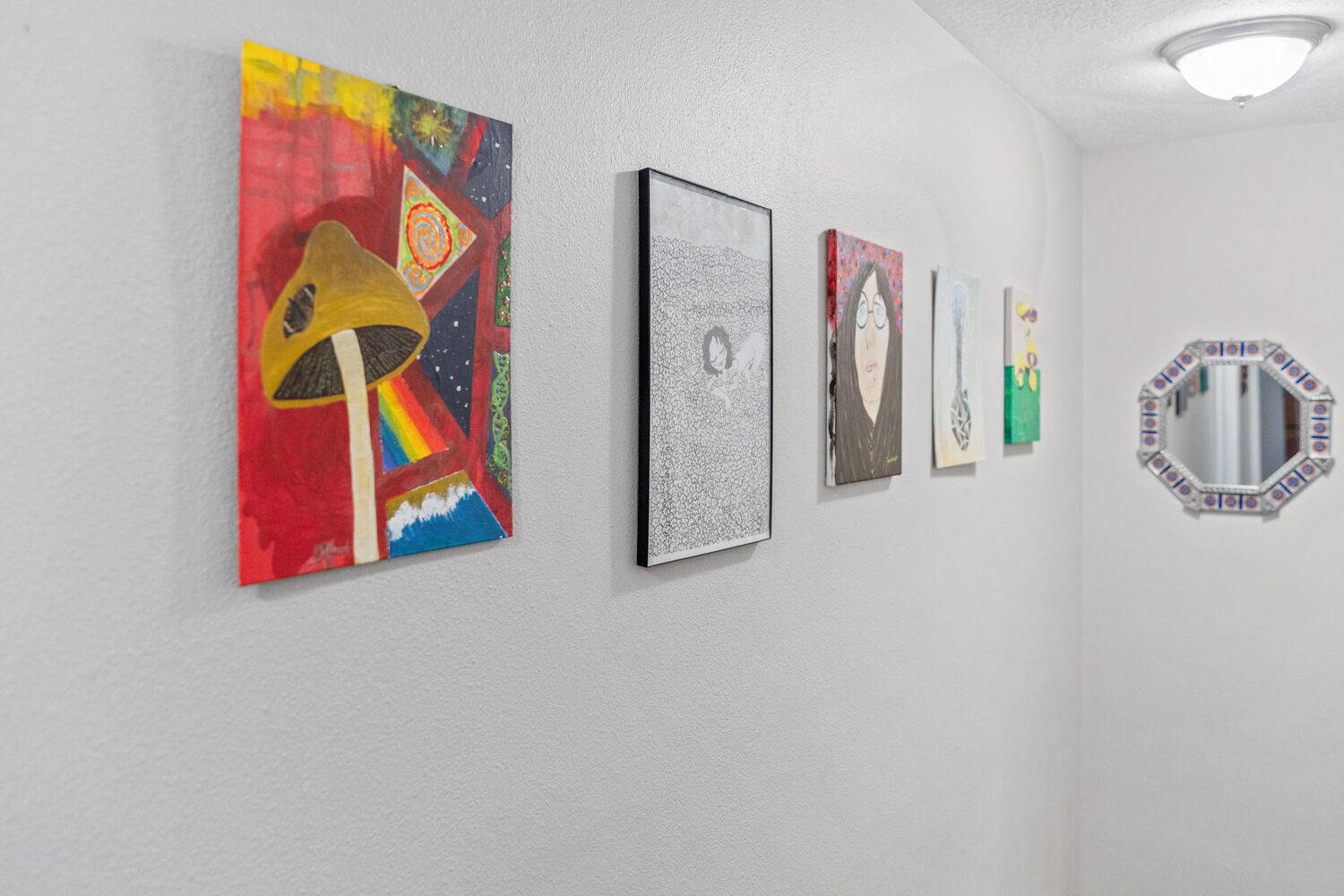 A hallway with a series of artworks on the wall, including a colorful abstract piece and a black and white textured artwork.