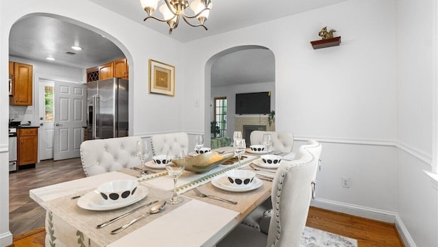 A dining area with a white table set for four, a chandelier, and a kitchen in the background. - Newly active beautiful 5-bedroom house in a prime location near DC (Arlington)