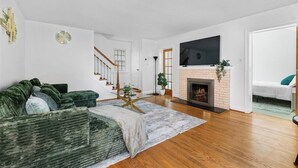A modern living room with a green sofa, a fireplace, a TV, and a staircase leading to another room. - Newly active beautiful 5-bedroom house in a prime location near DC (Arlington)