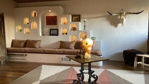 A cozy living room with a sofa, a coffee table with a vase of flowers, and a wall with multiple framed pictures and a cow skull decoration.