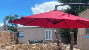 A stone patio with two blue lounge chairs and a red umbrella.