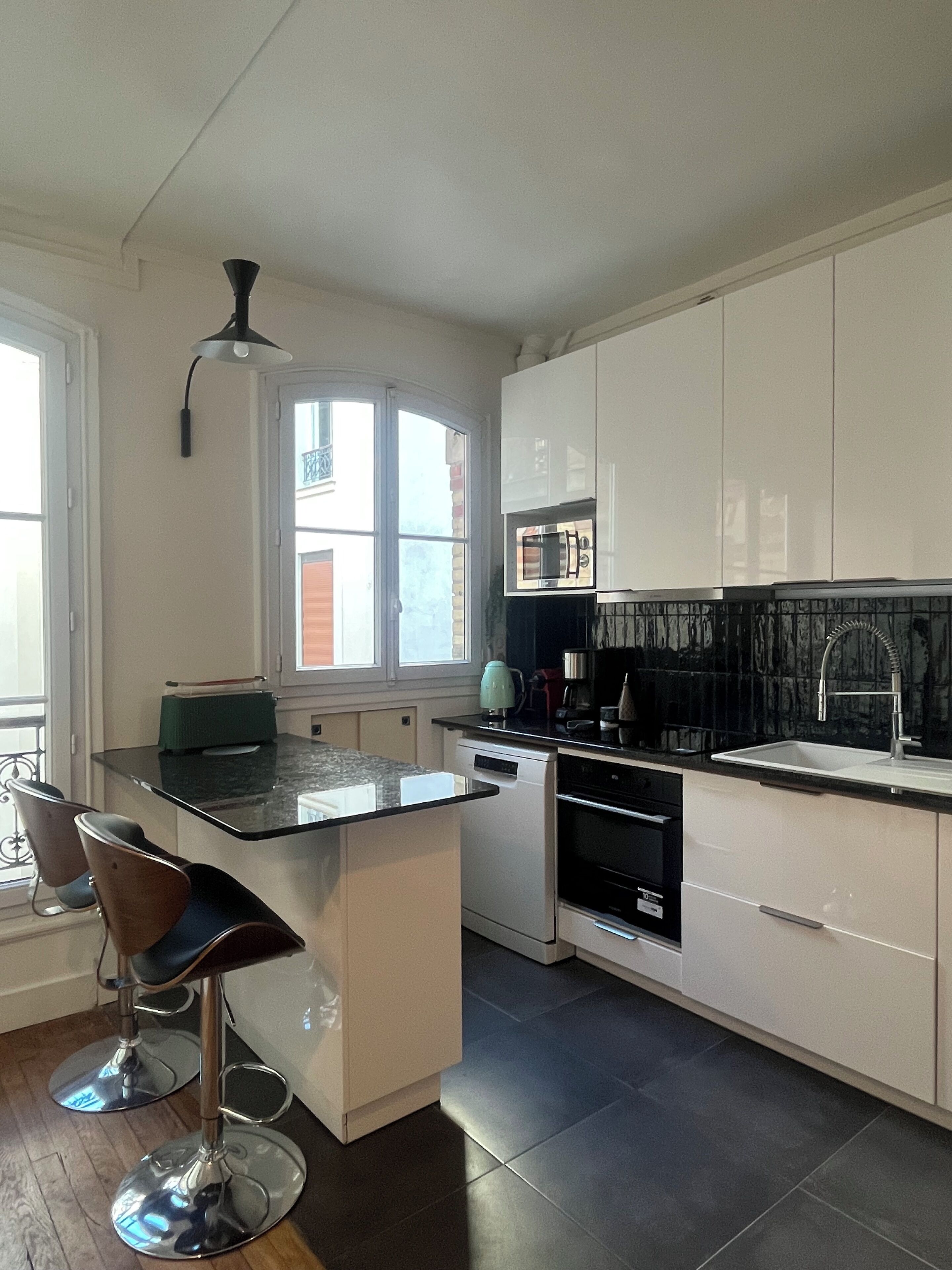 Una cocina moderna con armarios blancos, encimera negra y ventana que proporciona luz natural.