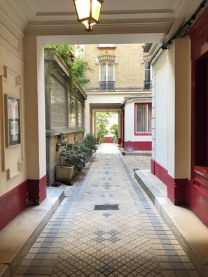 A narrow corridor with tiled flooring, a metal grate, and a hanging light fixture. - Cosy apartment in the heart of the XIth arrondissement, near Bastille (Paris)