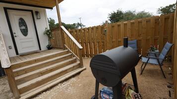 A backyard with a wooden deck, a barbecue grill, and a seating area with chairs.