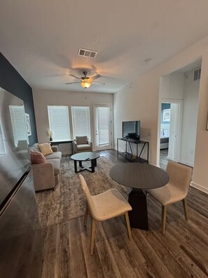 A modern living room with a flat-screen TV, a ceiling fan, and a dining area with a round table and chairs. - Comfy Get Away in Austin (Leander)