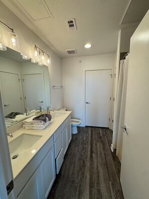 A bathroom with a white sink, mirror, and toilet, wooden flooring, and a shower curtain. - Comfy Get Away in Austin (Leander)