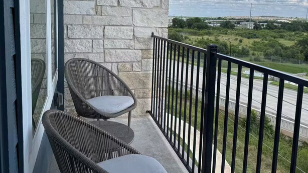 Een balkon met twee rieten stoelen en uitzicht op een weg en groen.