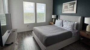 Een slaapkamer met een bed, een plafondventilator, een televisie en een raam met jaloezieën.