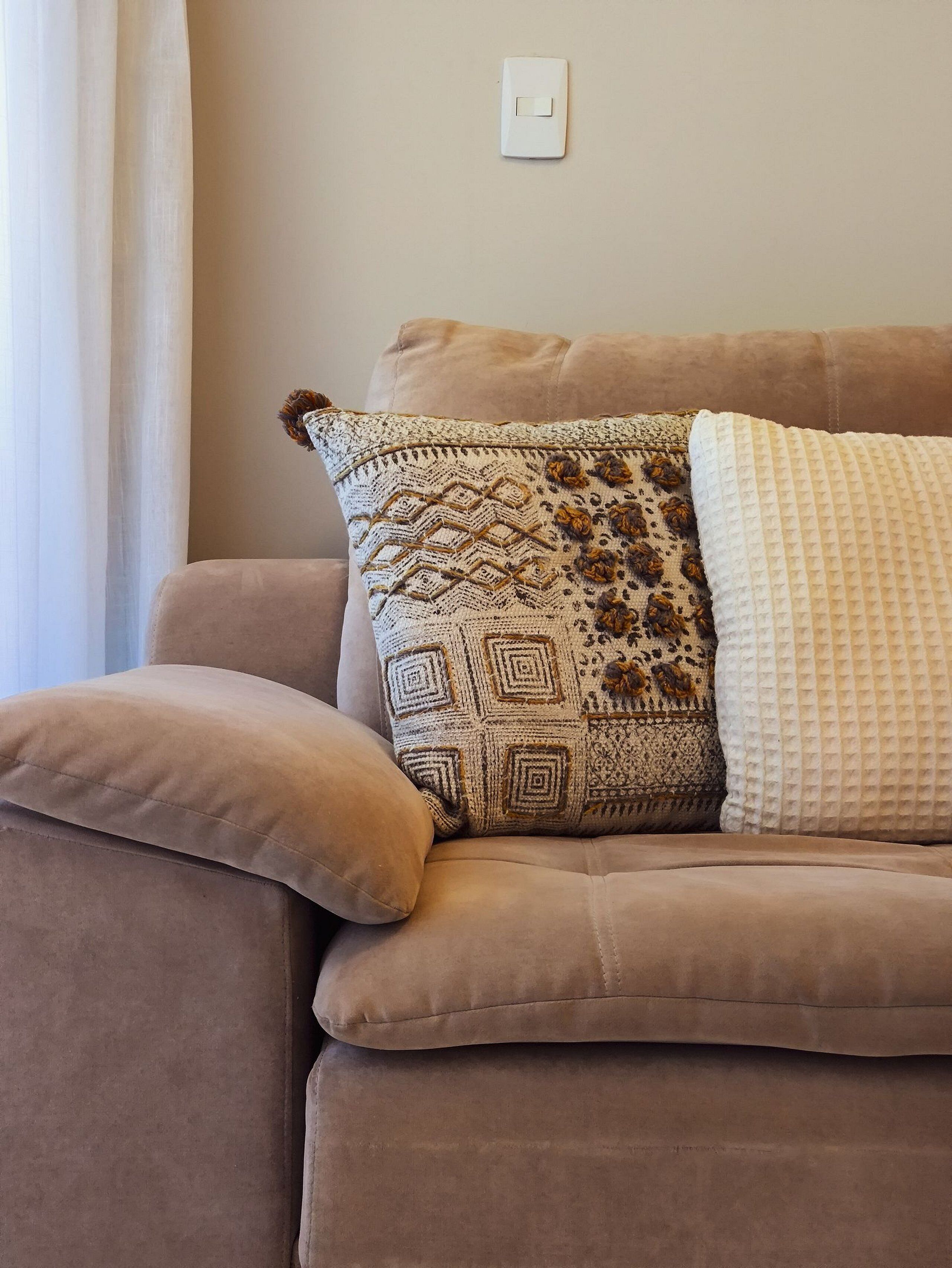 Ein beiges Sofa mit einem gemusterten Zierkissen und einem schlichten weißen Kissen.