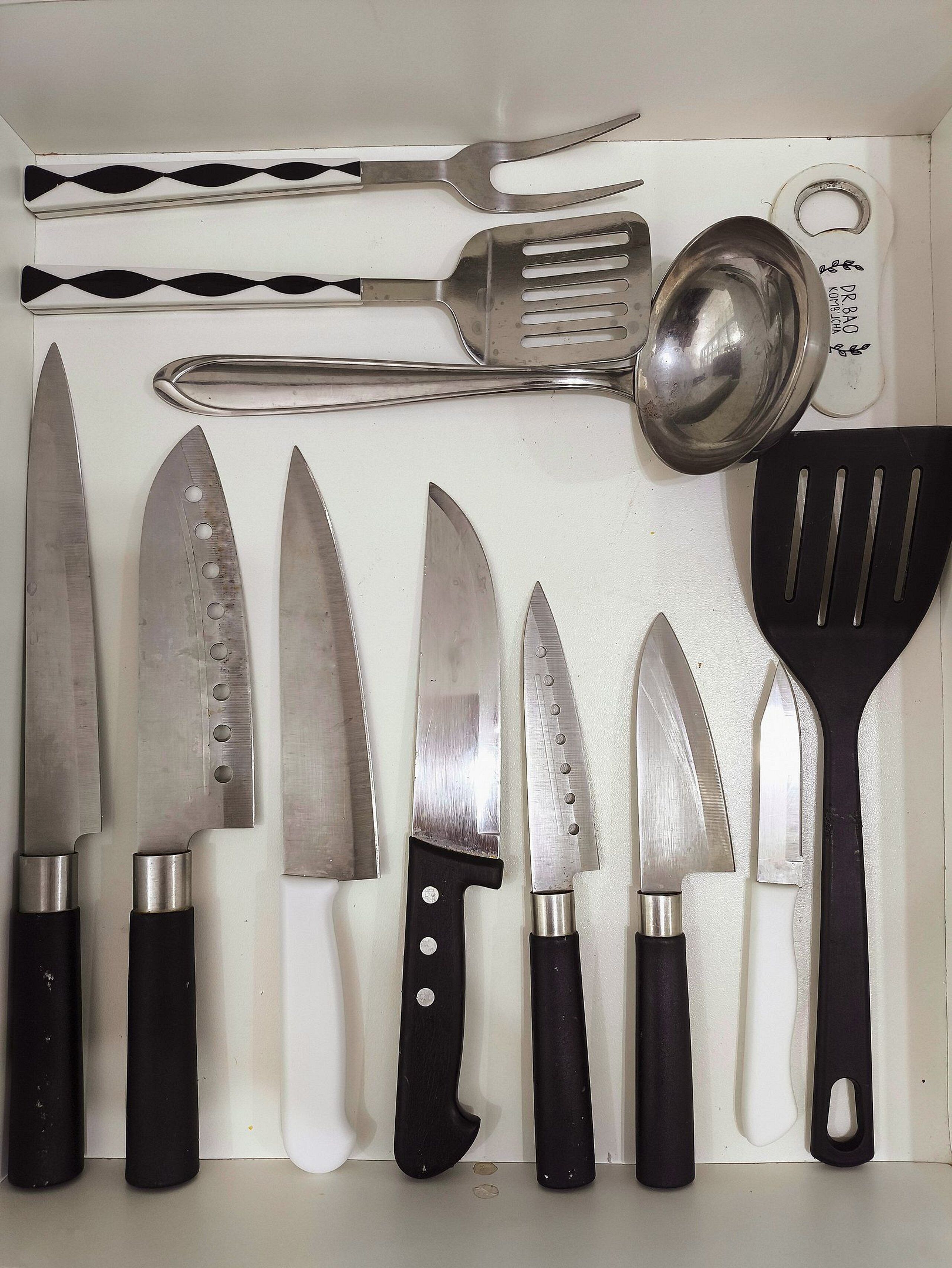 A drawer containing various kitchen utensils including knives, a spatula, and a grater.