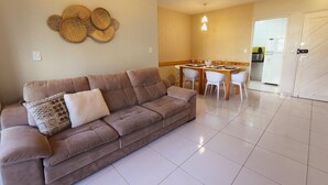 A living room with a brown sofa, a dining table with chairs, a kitchen in the background, and a door. - Tarantus (Joao Pessoa)