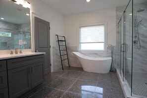 Un baño moderno con una bañera independiente, cabina de ducha de vidrio y tocador con un espejo grande.