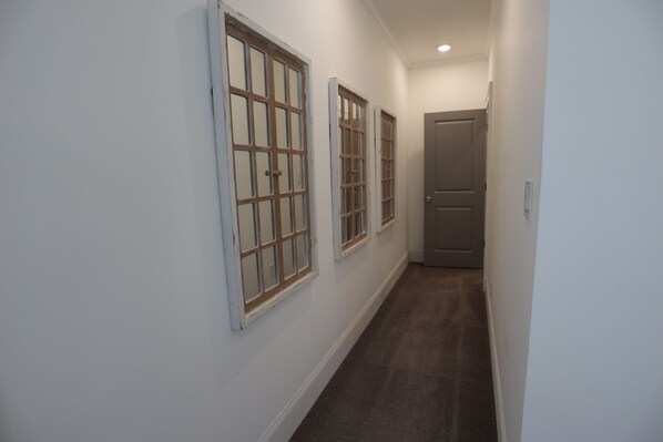 A narrow hallway with three windows on one side and a door at the end.