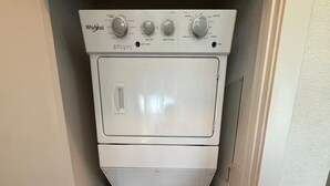 A compact, white Whirlpool washer and dryer unit in a narrow laundry room with wooden flooring. - Pleasant apartment in Austin (Leander)