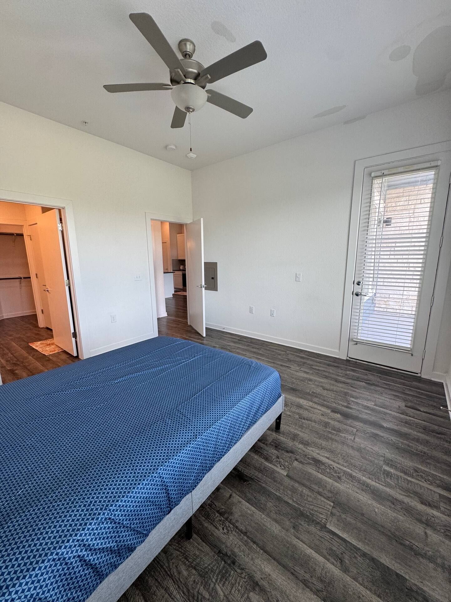 Un dormitorio con cama, ventilador de techo y puerta que da a un pasillo.