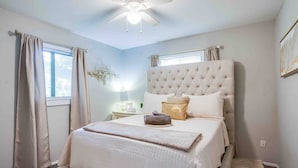 Een slaapkamer met een groot bed, een plafondventilator en een nachtkastje met een lamp.