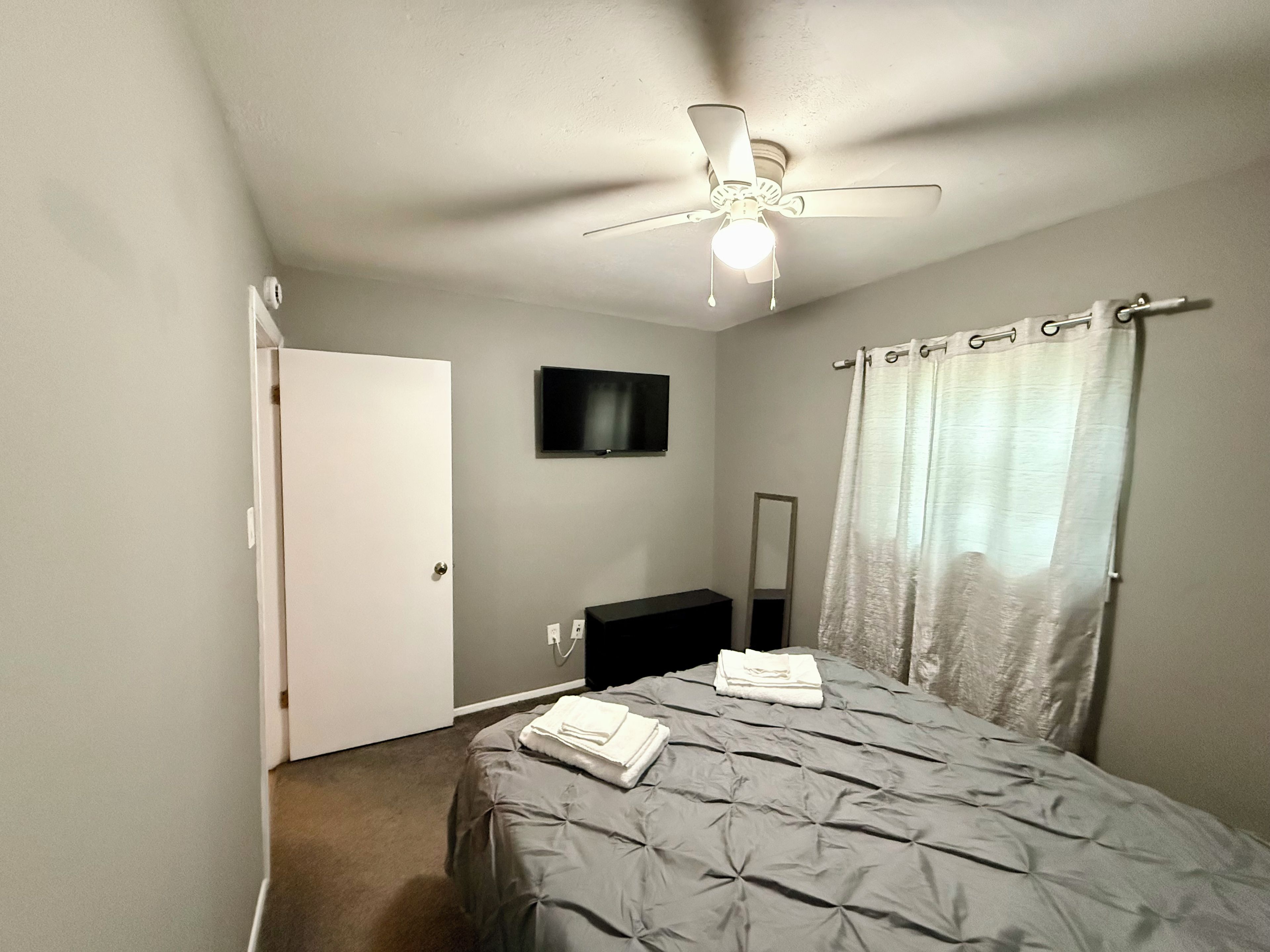 Une chambre à coucher avec un lit, un ventilateur de plafond, une télévision, un miroir et un rideau de douche.