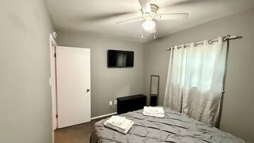 Une chambre à coucher avec un lit, un ventilateur de plafond, une télévision, un miroir et un rideau de douche.