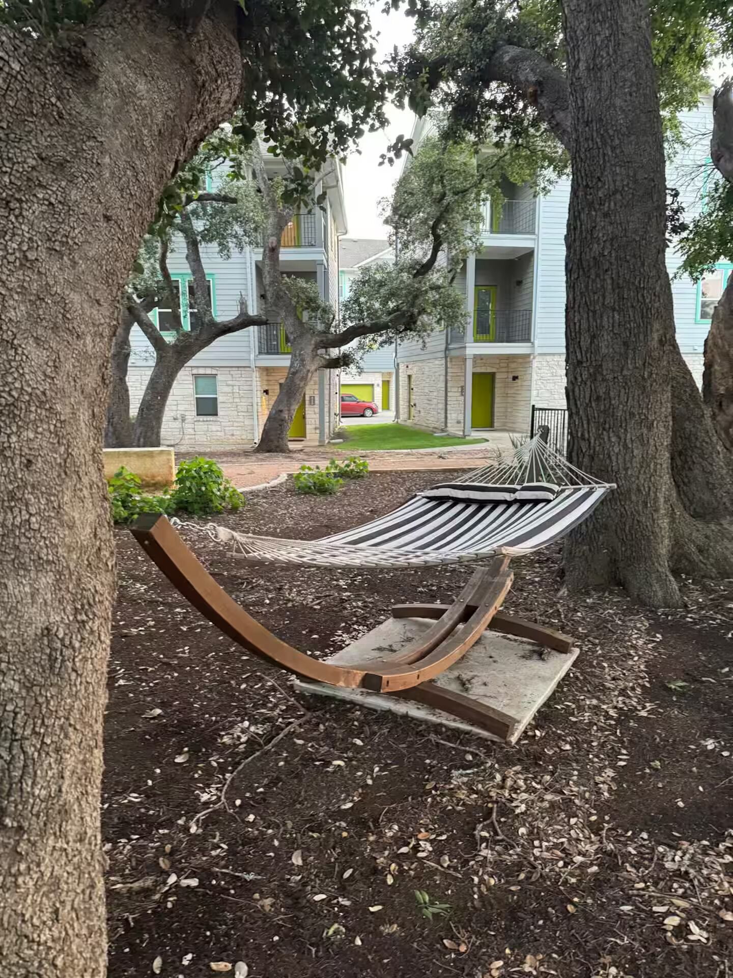 A hammock in a park area with trees and a building in the background.