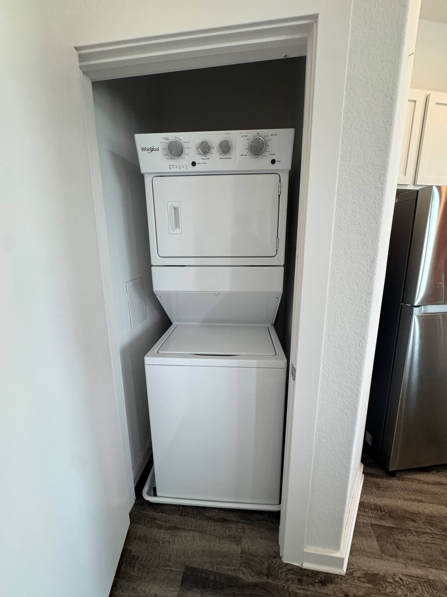 A compact washer and dryer unit in a small laundry room with a wooden floor.