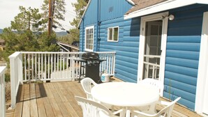 Uma casa azul com deck de madeira, churrasqueira e uma mesa branca com cadeiras.