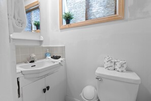 Une salle de bain avec un lavabo blanc, des toilettes et une fenêtre donnant sur un mur de briques.