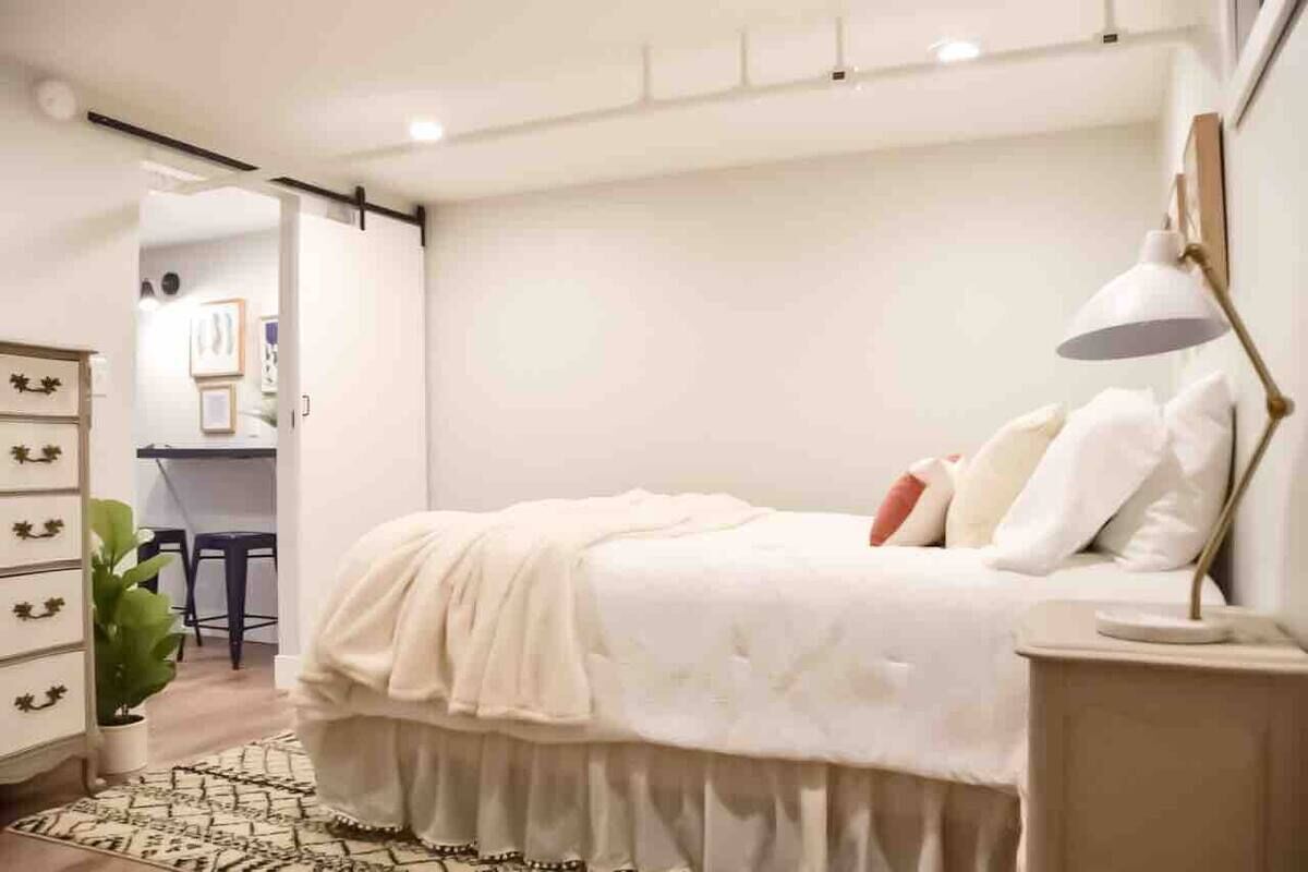 A modern bedroom with a bed, bedside table, lamp, and a potted plant.