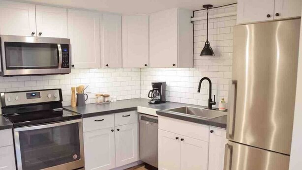 Una cocina moderna con electrodomésticos de acero inoxidable, armarios blancos y salpicadero de azulejos.