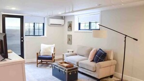 Una sala de estar con un sofá, una silla, una mesita, una lámpara de pie y una maleta.