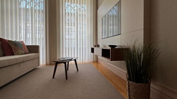 Ein modernes Wohnzimmer mit einer Couch, einem Couchtisch, einem an der Wand montierten Fernseher und einer Topfpflanze.