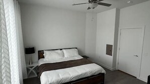 Un dormitorio con cama, ventilador de techo, mesita de noche y una puerta.