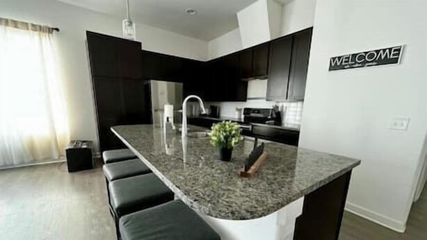 Una cocina moderna con una isla central, armarios negros y un letrero que dice 'WELCOME'.