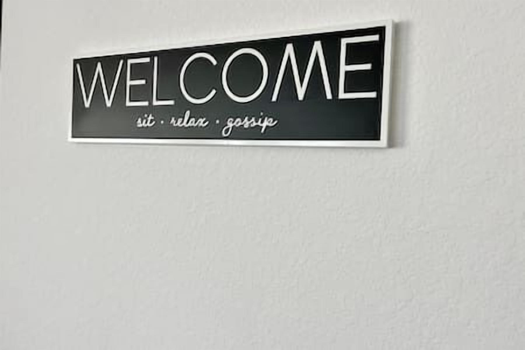 A welcome sign with the words 'WELCOME sit relax gossip' on a wall.