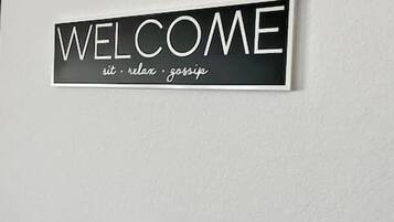A welcome sign with the words 'WELCOME sit relax gossip' on a wall.