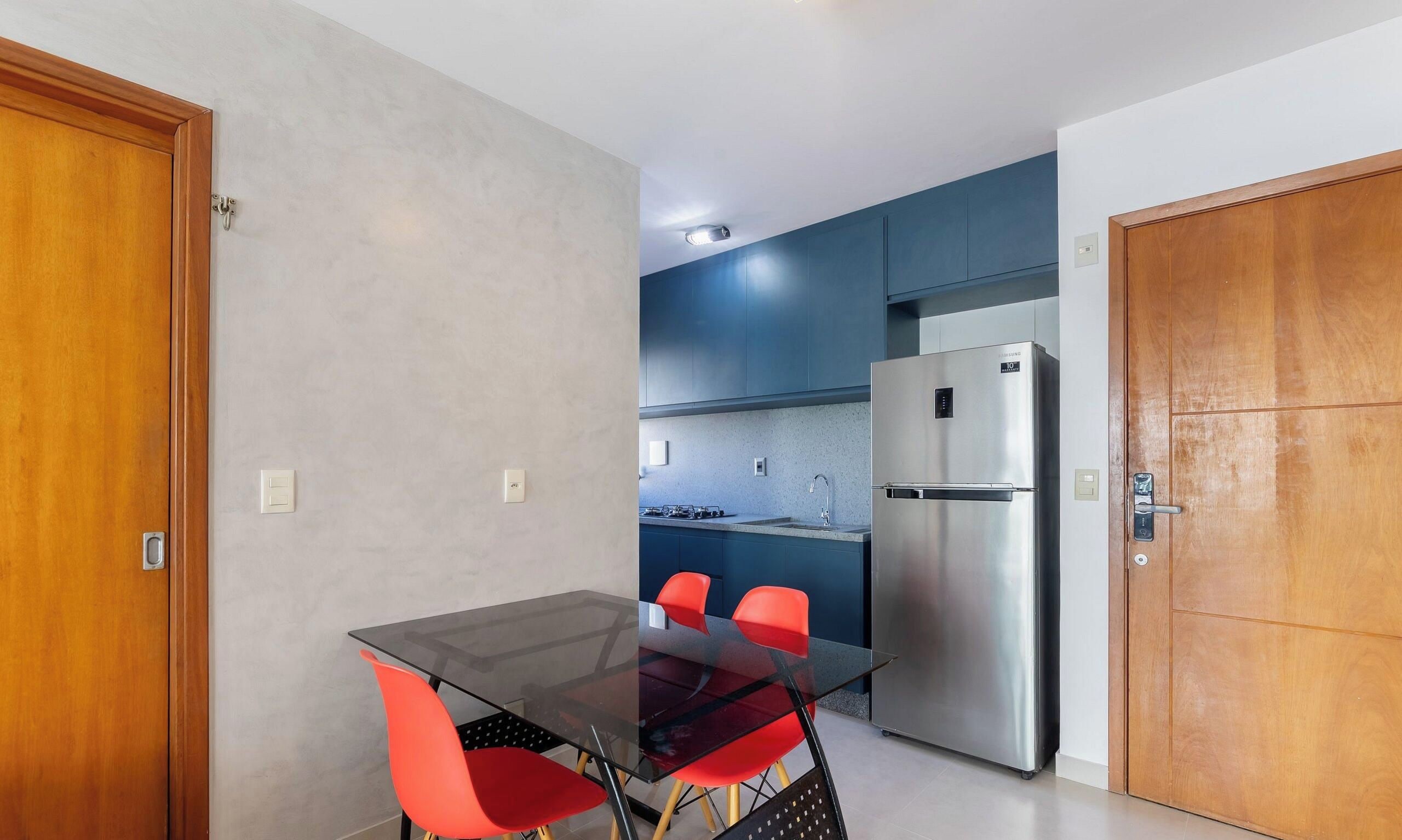 Una cocina funcional con refrigerador, una mesa de comedor con sillas y una puerta de madera.