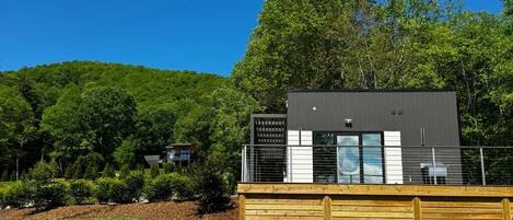 A modern building with a wooden deck, surrounded by lush greenery and a clear blue sky.