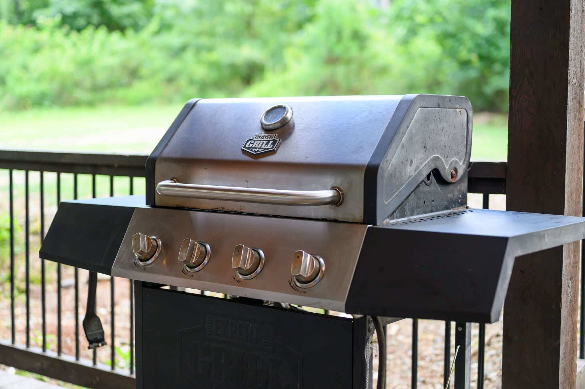 Una parrilla para barbacoa con cuatro quemadores y una repisa lateral, montada sobre un soporte de metal.