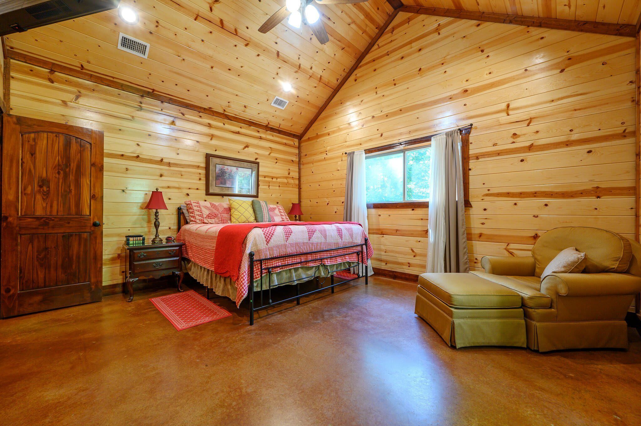 A cozy wooden cabin bedroom with a bed, a chair, a nightstand, and a window.