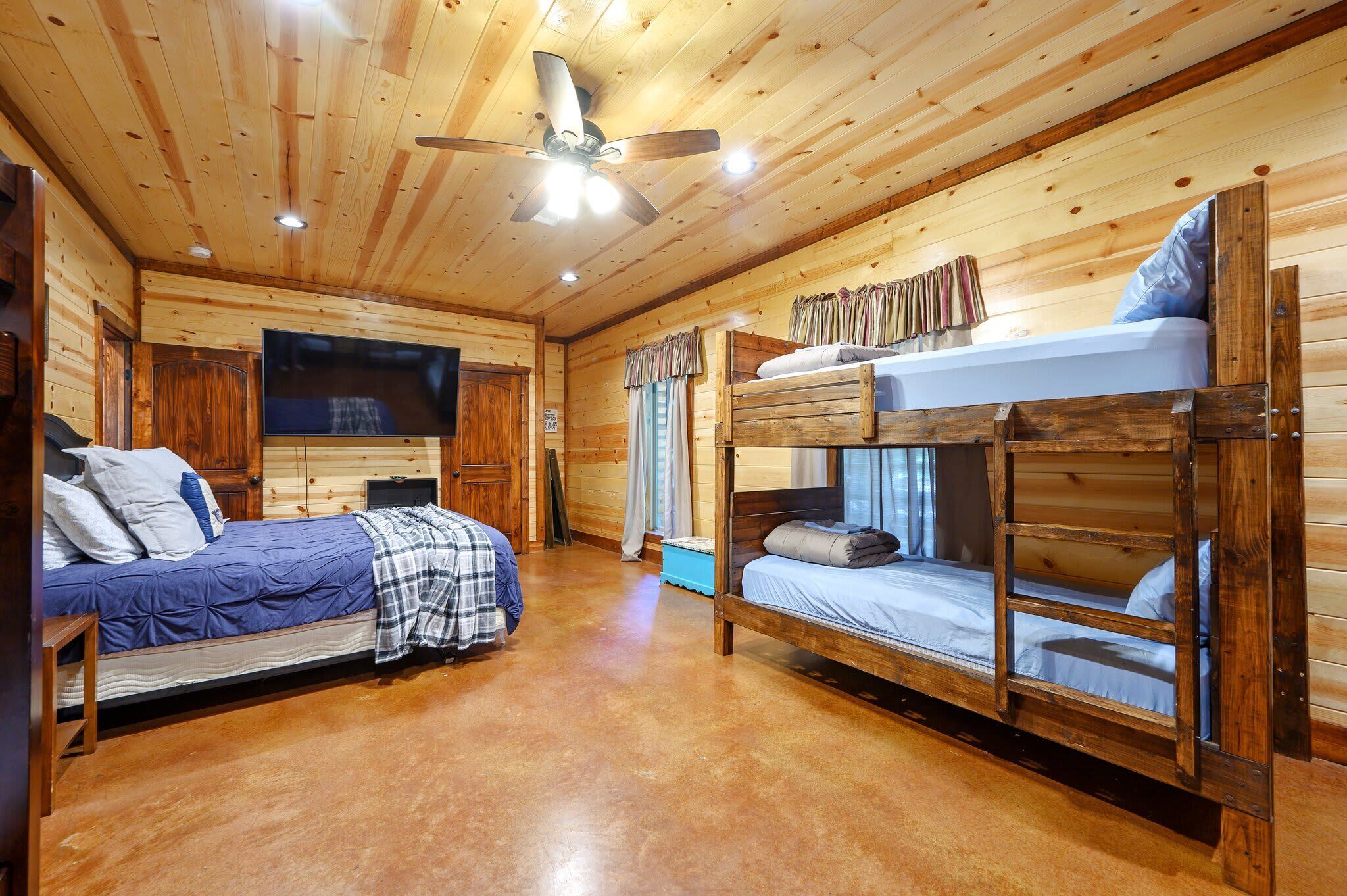Une chambre de style cabane avec deux lits superposés, un ventilateur de plafond et un téléviseur à écran plat.