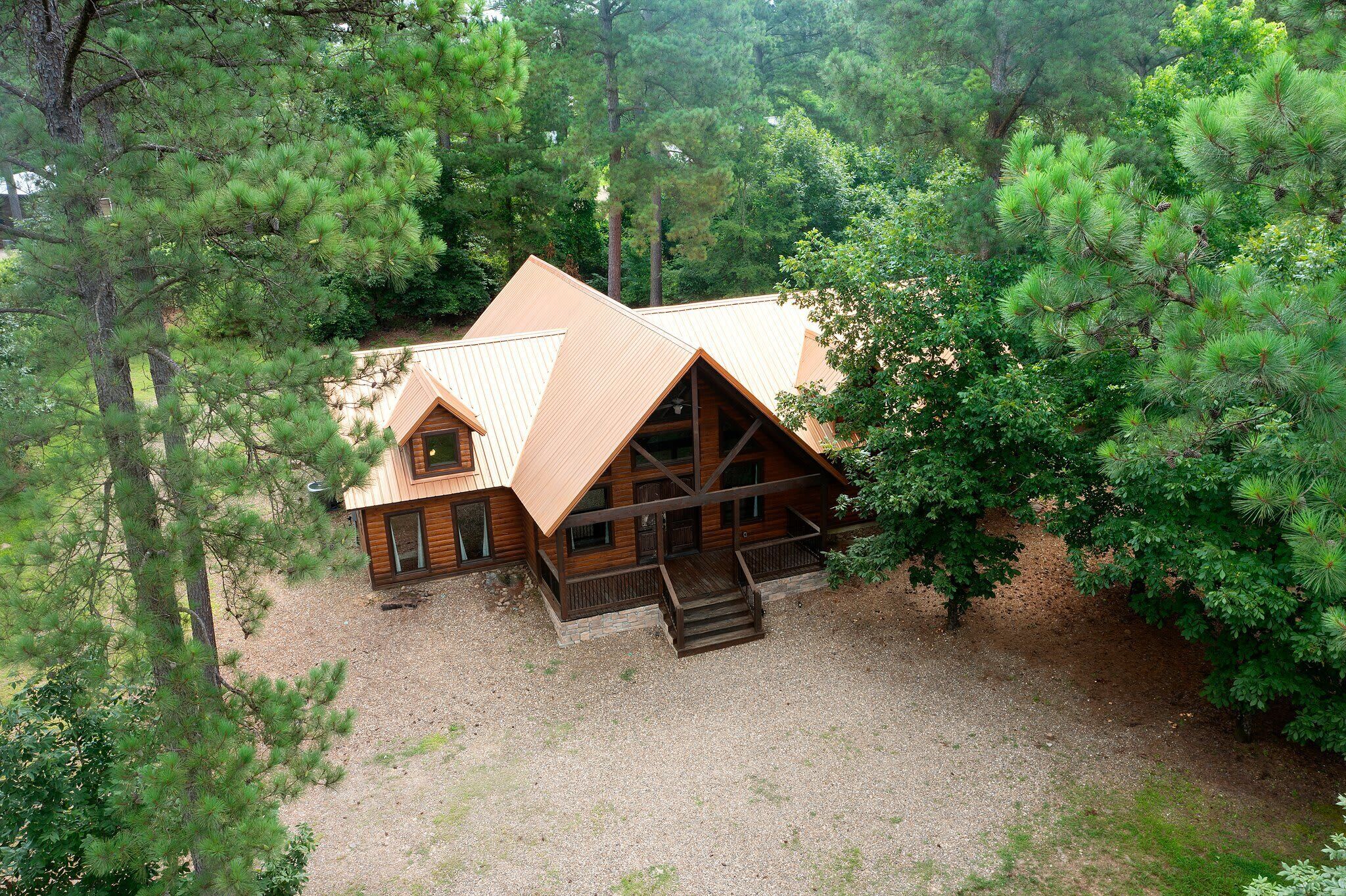 A cabin with a sloped roof, wooden exterior, and a gravel driveway surrounded by dense trees.