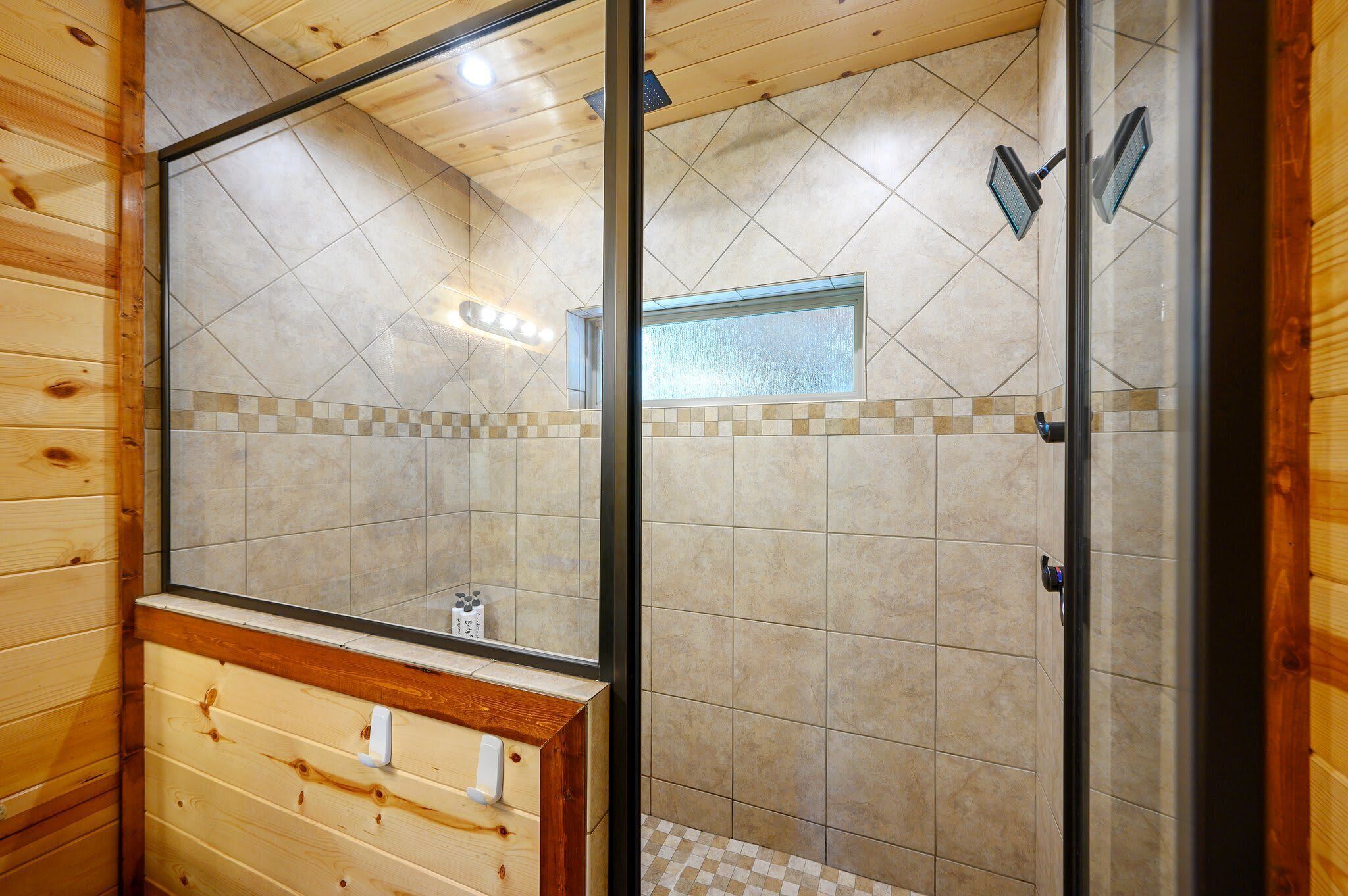Un baño con paneles de madera, cabina de ducha de vidrio, piso de baldosas y tocador de madera.