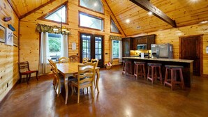 A wooden cabin interior with a dining area, kitchen, and large windows.